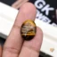 Oval tiger eye gemstone held between person's thumb and finger