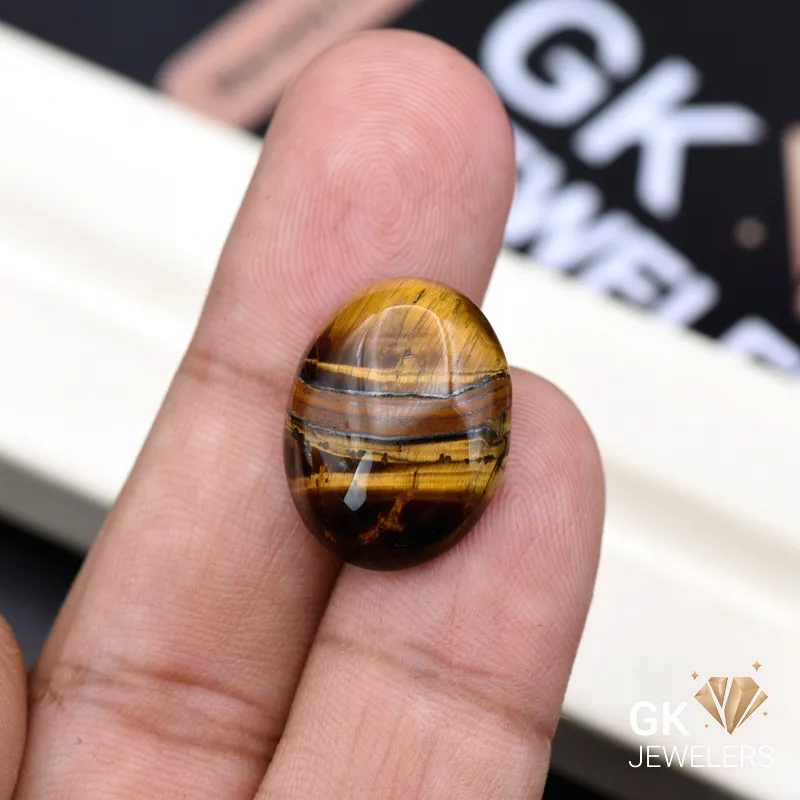 Oval tiger eye gemstone held between person's thumb and finger