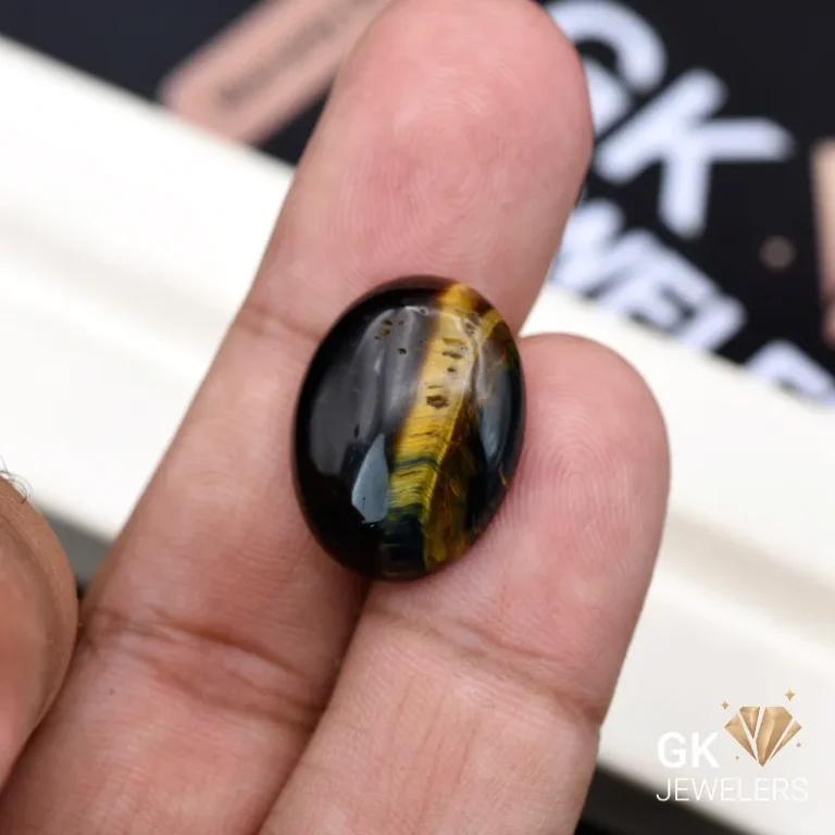 Oval tiger eye gemstone held between person's thumb and index finger