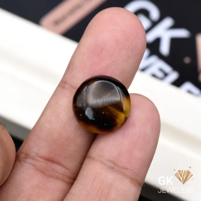 Round tiger eye gemstone held between person's thumb and index finger