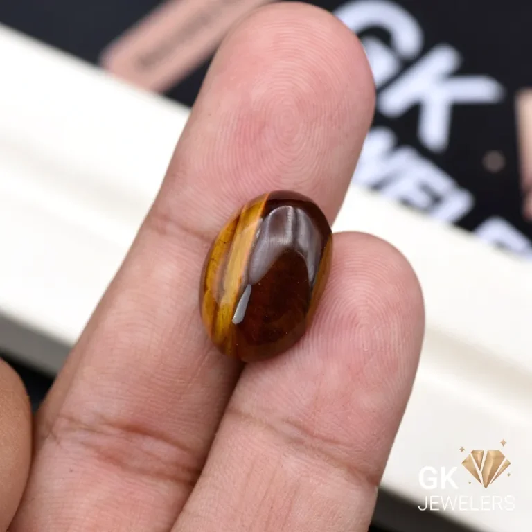 Oval tiger eye gemstone held between person's thumb and finger