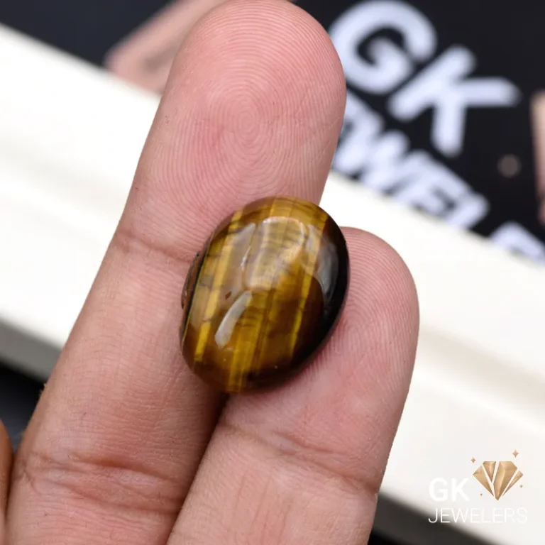 Oval tiger eye gemstone held between person's thumb and finger