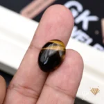 Oval tiger's eye gemstone held between person's thumb and fingers