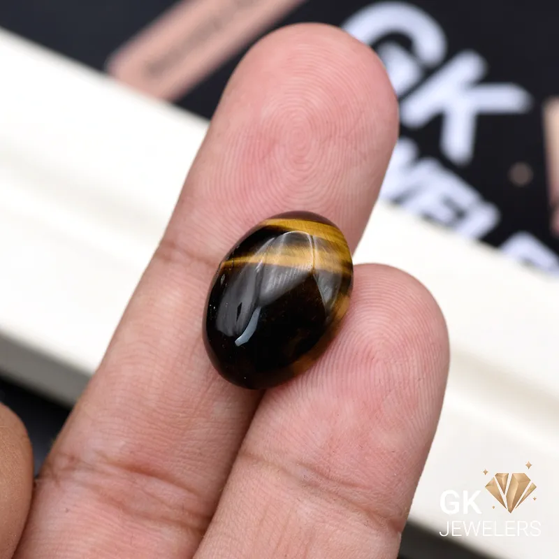 Oval tiger's eye gemstone held between person's thumb and fingers