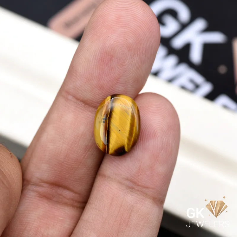 Oval tiger eye gemstone held between person's thumb and fingers