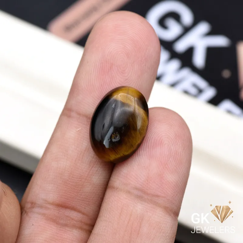Oval tiger's eye gemstone held between person's thumb and finger