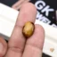 Oval tiger's eye gemstone held between person's thumb and index finger