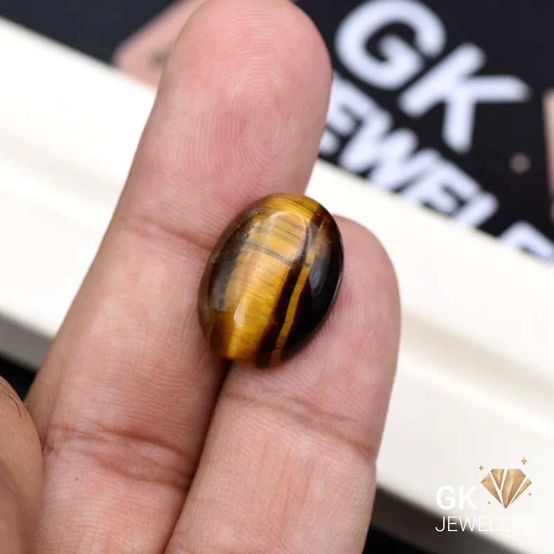 Oval tiger eye gemstone with golden chatoyancy held between fingers