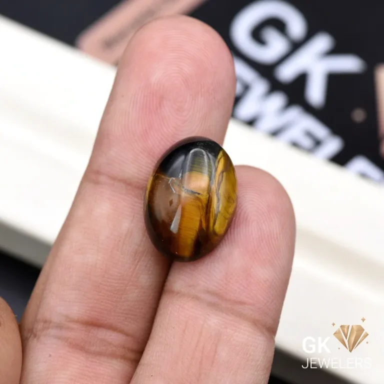 Oval tiger eye gemstone held between person's fingers showing golden bands