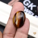 Oval tiger eye gemstone held between person's thumb and index finger